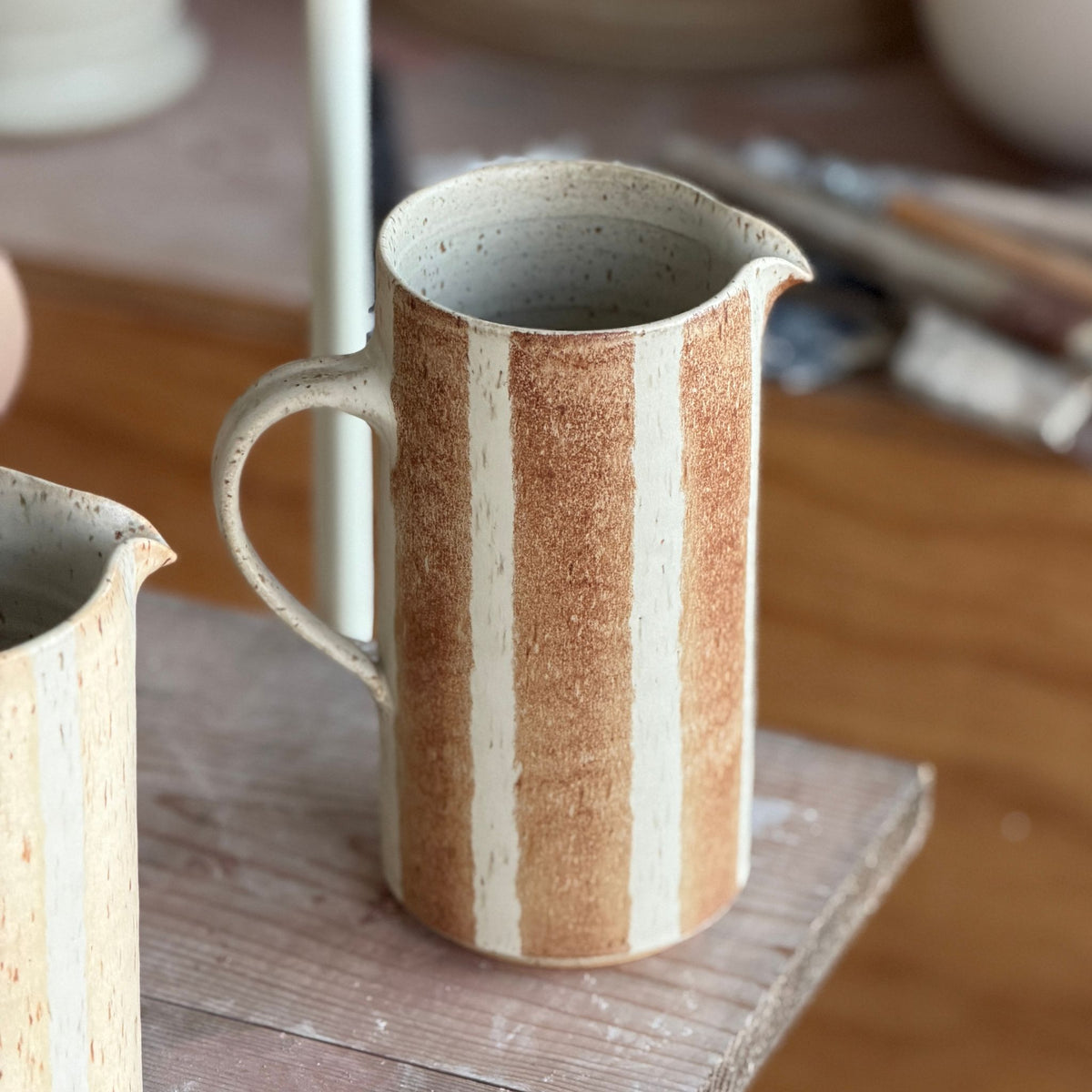 Handgjord randig keramikkanna i brun glasyr på havrefärgad botten från Paradisverkstaden, cirka 20 cm hög.