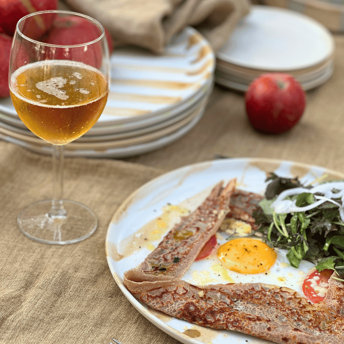Galette med sallad och ägg på en randig tallrik tillsammans med fransk cider